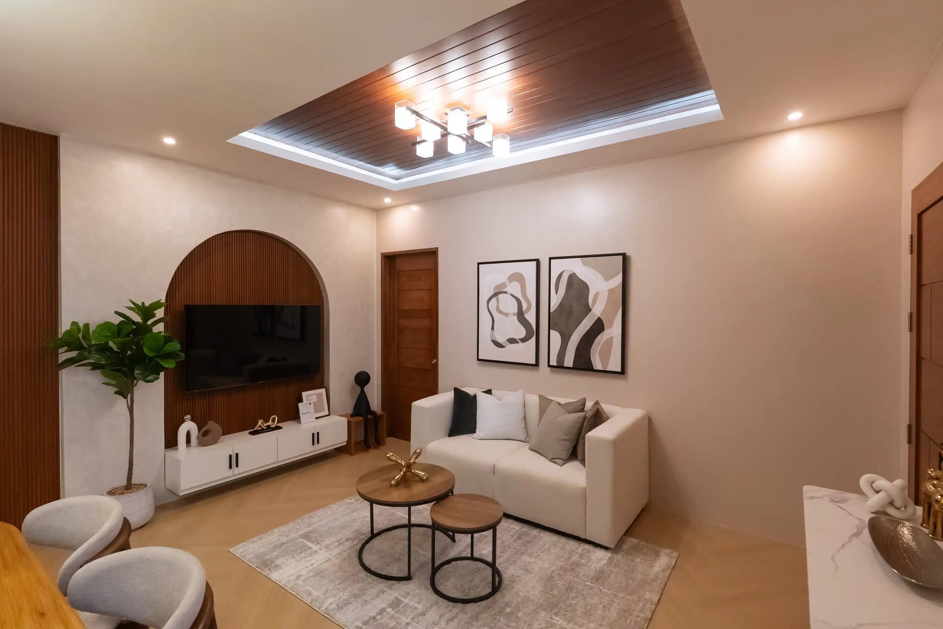 Modern minimalist abstract diptych canvas prints showcased in a real home installation, featuring organic fluid shapes, thick interlocking blocks, and bold curving outlines in beige, cream white, taupe brown, and black hanging above a living room sofa.