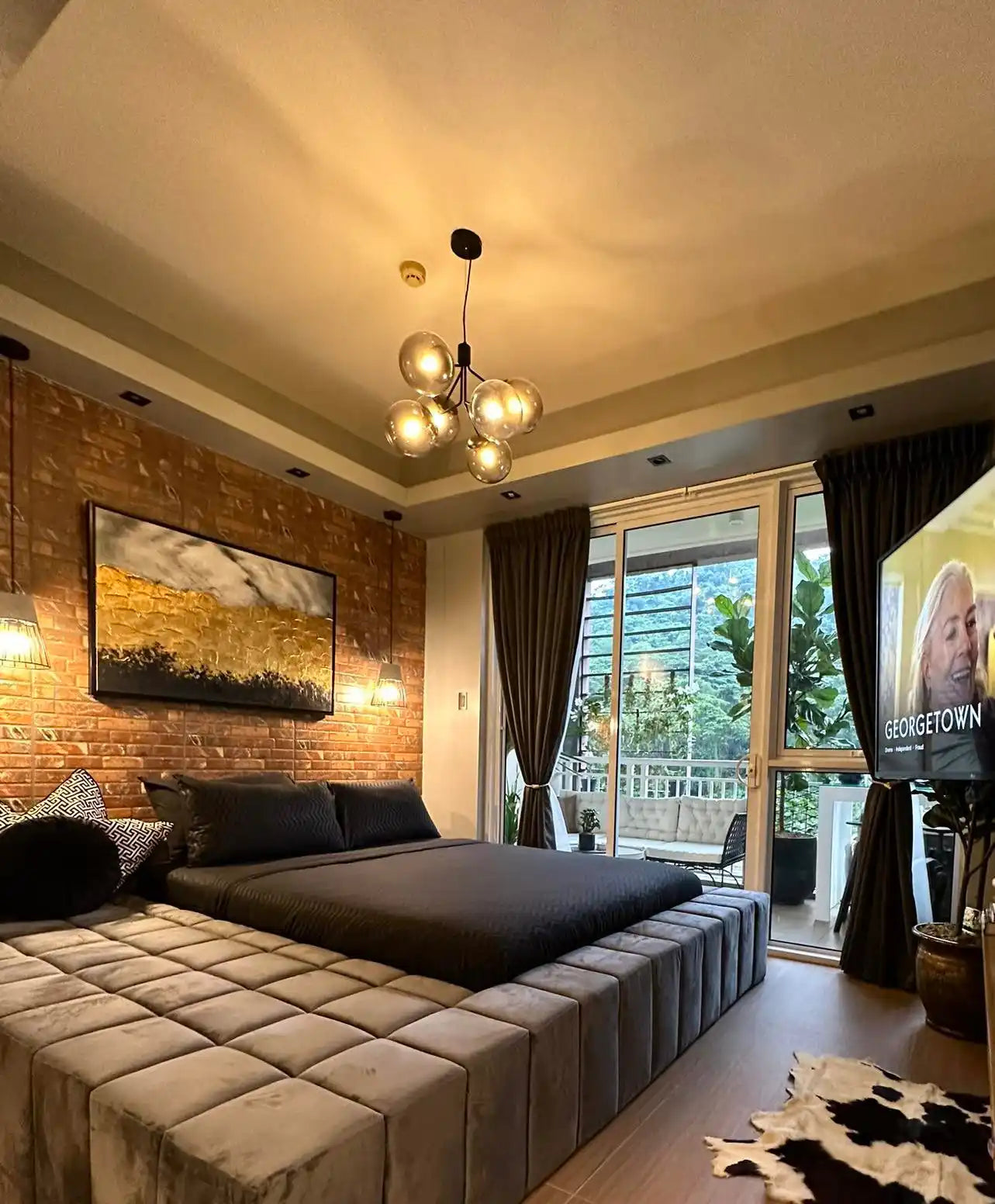 Oversized modern minimalist abstract landscape canvas print showcased in a real bedroom installation, featuring a textured golden horizon line and deep black fields hanging on an exposed brick accent wall above a luxury platform bed